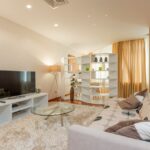 Glass round coffee table placed on soft fur rug between comfortable sofa and modern TV set in spacious living room